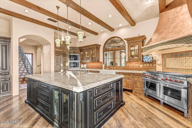 kitchen with light wood-style flooring, appliances with stainless steel finishes, dark cabinetry, backsplash, and a large island with sink