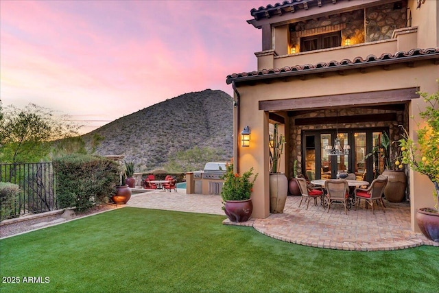 10935 E Grandview Way, Scottsdale, AZ 85255 - back of property at dusk featuring fence, exterior kitchen, a patio area, a fireplace, and a mountain view