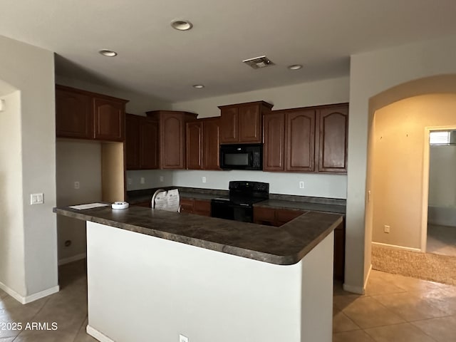 kitchen with light tile patterned flooring, dark brown cabinets, a center island with sink, and black appliances