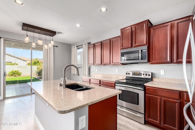 kitchen with pendant lighting, sink, stainless steel appliances, light stone countertops, and an island with sink