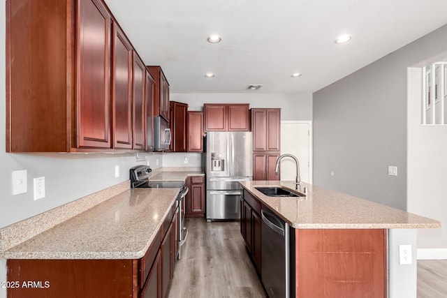 kitchen with sink, stainless steel appliances, light stone counters, a center island with sink, and light wood-type flooring