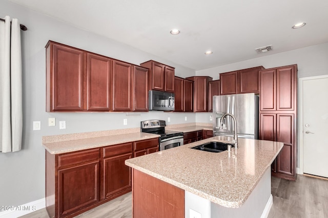 kitchen with sink, a center island with sink, light wood-type flooring, appliances with stainless steel finishes, and light stone countertops