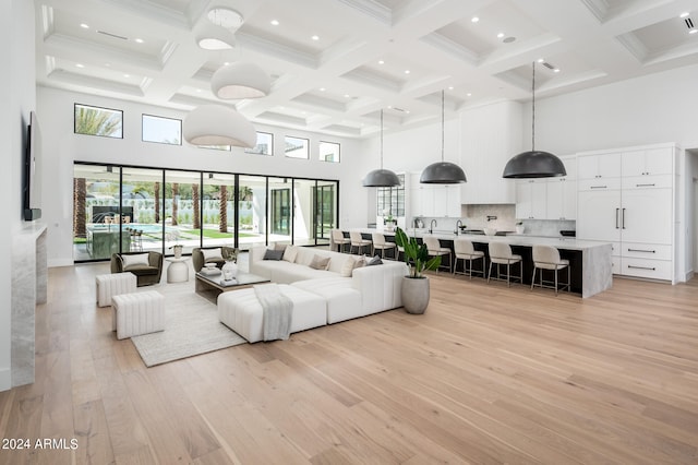 living room featuring light wood-type flooring, beamed ceiling, a high ceiling, and coffered ceiling