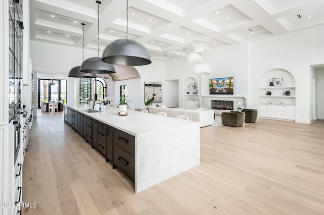 kitchen with light hardwood / wood-style flooring, a towering ceiling, an island with sink, and hanging light fixtures