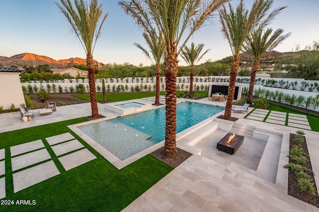 pool at dusk featuring a mountain view, a patio, an in ground hot tub, and an outdoor fire pit