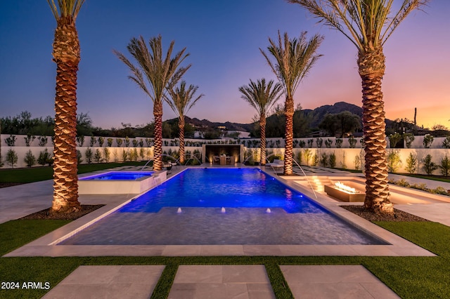 pool at dusk featuring a patio, an in ground hot tub, and pool water feature