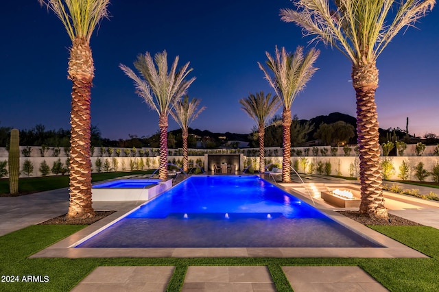 pool at dusk featuring an in ground hot tub, pool water feature, and a patio area