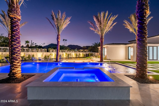 pool at dusk with an in ground hot tub, pool water feature, and a patio area