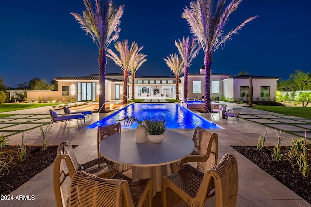 pool at night featuring a patio area