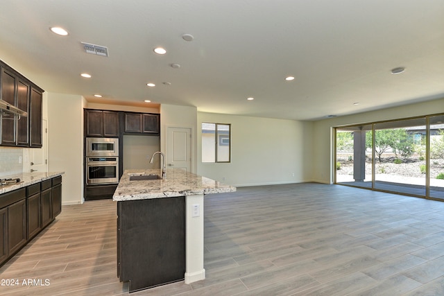 kitchen with stainless steel appliances, a kitchen island with sink, sink, and light wood-type flooring