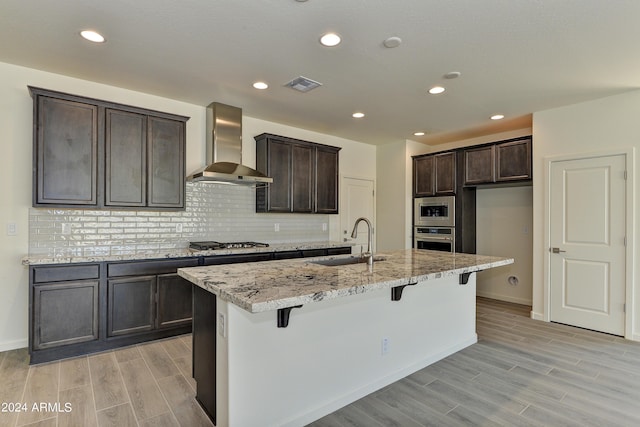 4320 Sawbuck Way, Wickenburg, AZ 85390 - kitchen featuring light wood-type flooring, wall chimney exhaust hood, appliances with stainless steel finishes, and a sink