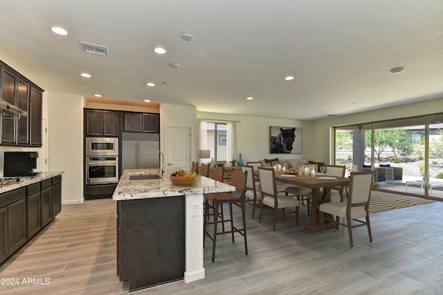 kitchen featuring an island with sink, sink, built in appliances, a breakfast bar, and light hardwood / wood-style floors