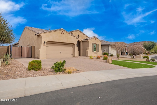 mediterranean / spanish-style house featuring stucco siding, an attached garage, a gate, driveway, and a tiled roof