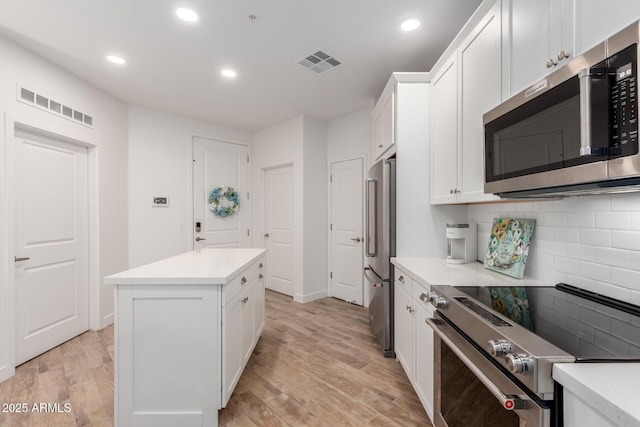 2511 W Queen Creek Rd Unit 174, Chandler, AZ 85248 - kitchen with stainless steel appliances, backsplash, white cabinets, light wood-style flooring, and a kitchen island