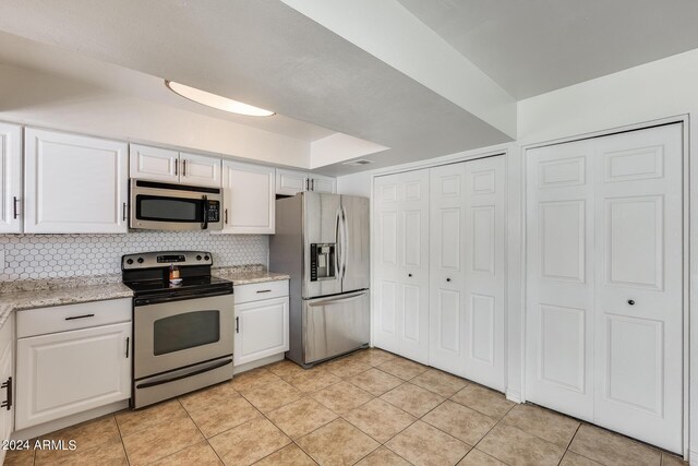 kitchen featuring white cabinets, light stone countertops, stainless steel appliances, light tile patterned flooring, and decorative backsplash