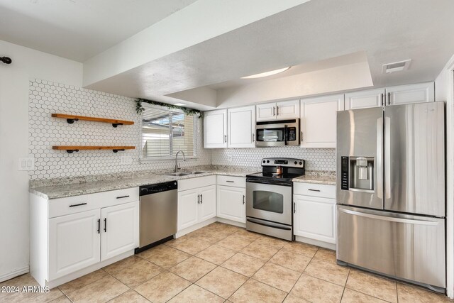 kitchen featuring tasteful backsplash, light stone counters, sink, appliances with stainless steel finishes, and white cabinets