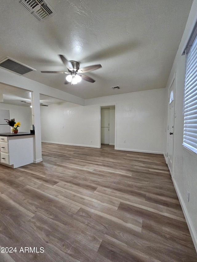 unfurnished living room featuring built in desk, hardwood / wood-style floors, a textured ceiling, and ceiling fan