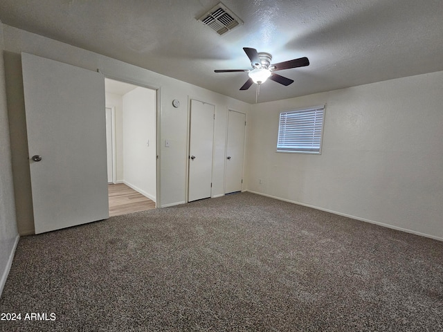 unfurnished bedroom featuring light colored carpet, ceiling fan, a textured ceiling, and two closets