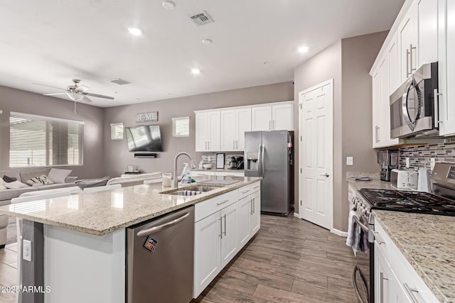 kitchen featuring white cabinets, appliances with stainless steel finishes, open floor plan, a kitchen island with sink, and a sink