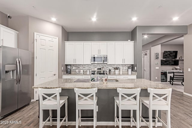 kitchen featuring stainless steel appliances, light stone countertops, a kitchen island with sink, and white cabinets