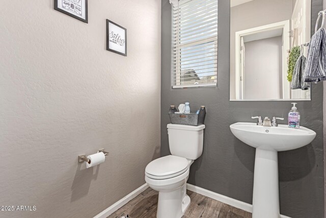 half bath with baseboards, toilet, and wood finished floors