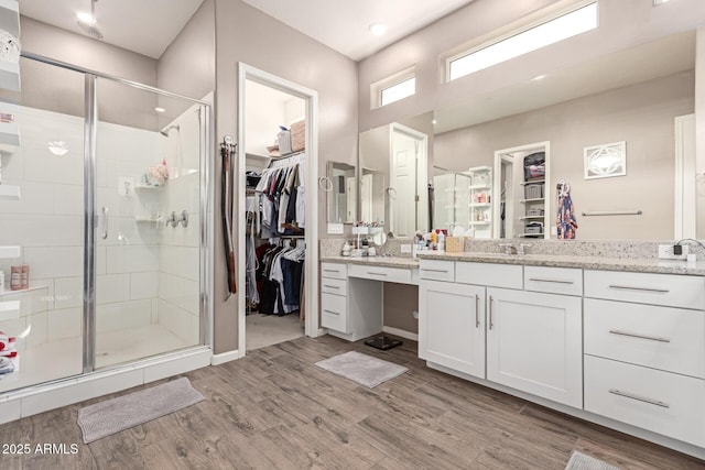 full bath featuring a shower stall, a walk in closet, wood finished floors, and vanity