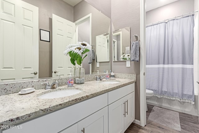 full bathroom with double vanity, toilet, a sink, and wood finished floors