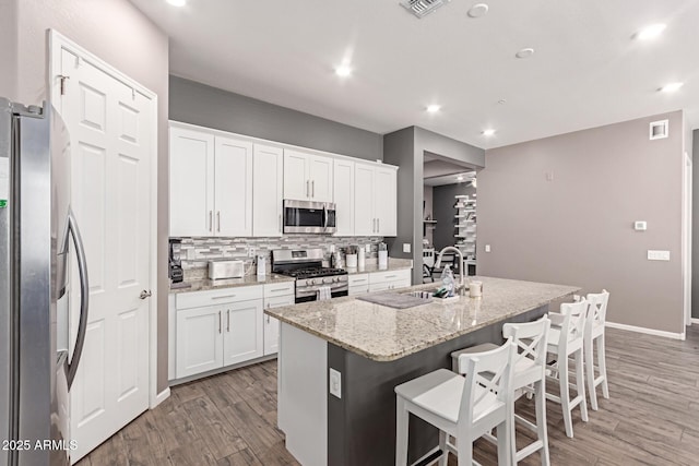 kitchen featuring white cabinetry, a kitchen island with sink, appliances with stainless steel finishes, and light stone counters