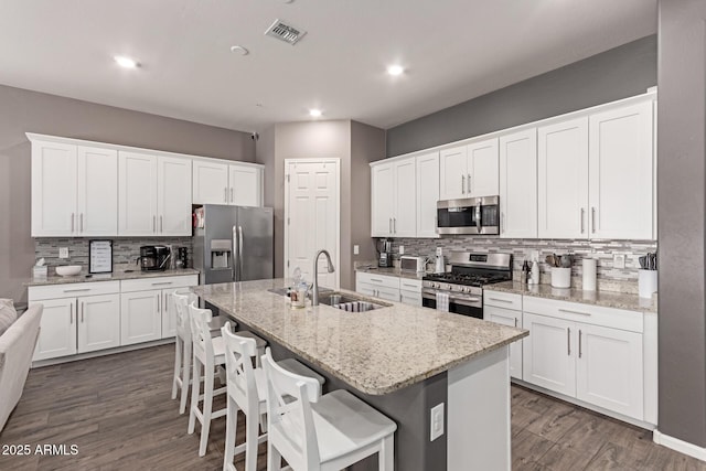 kitchen with a sink, visible vents, white cabinetry, appliances with stainless steel finishes, and an island with sink