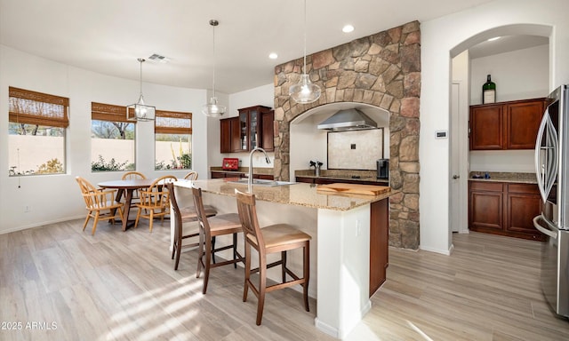 kitchen with stainless steel fridge, light wood-type flooring, sink, pendant lighting, and a center island with sink