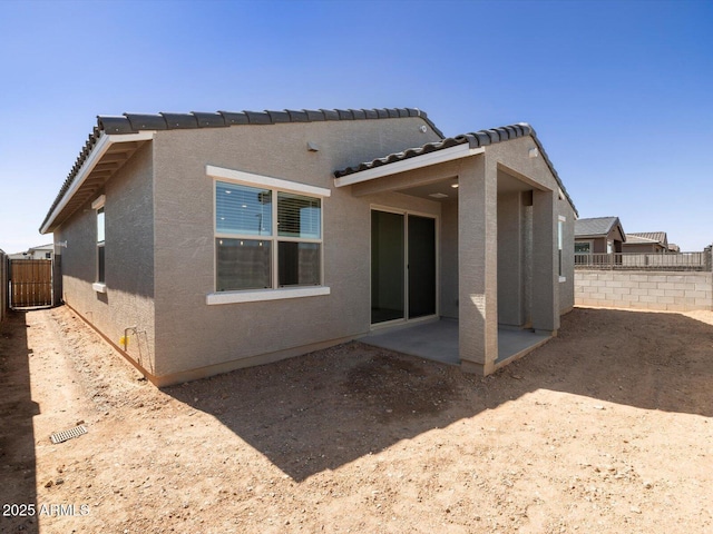 rear view of house with stucco siding, a patio, and fence