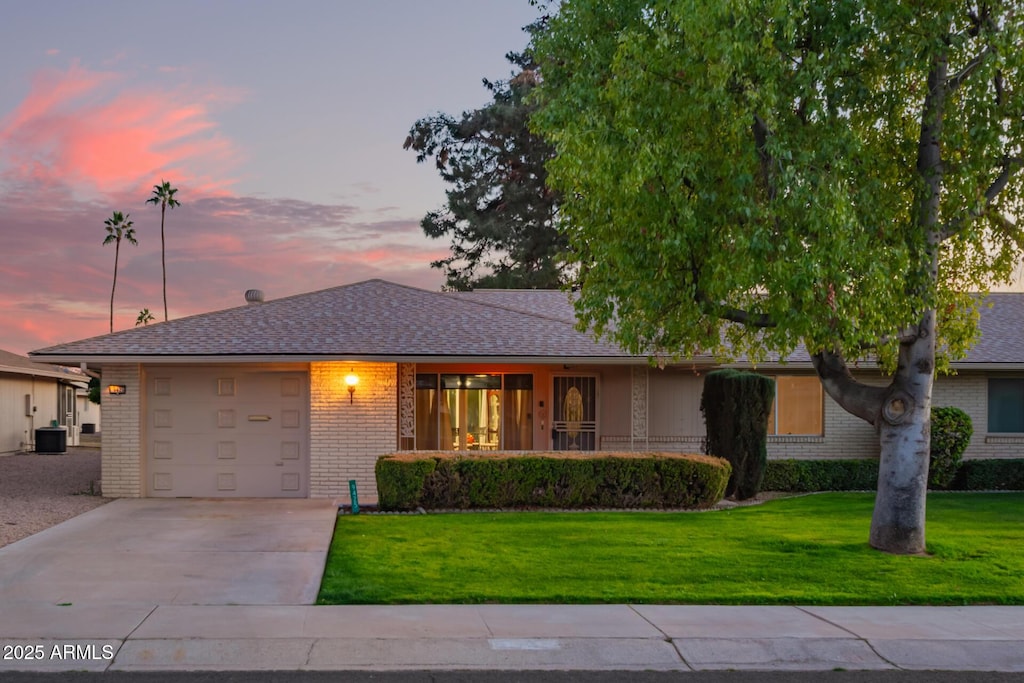 ranch-style home featuring a garage, a lawn, and central air condition unit