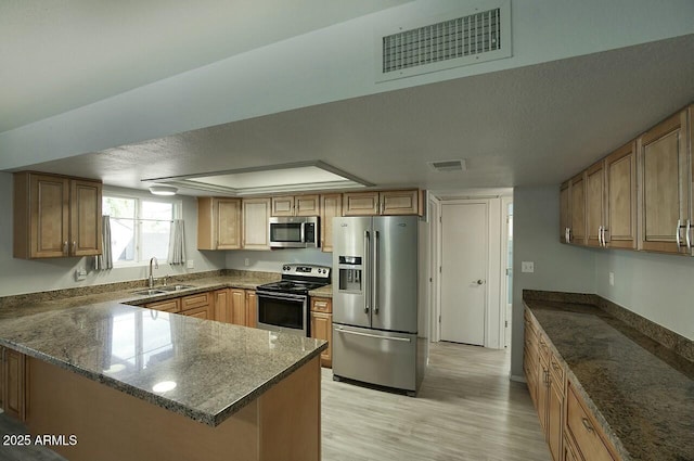 kitchen with sink, appliances with stainless steel finishes, a textured ceiling, kitchen peninsula, and light wood-type flooring