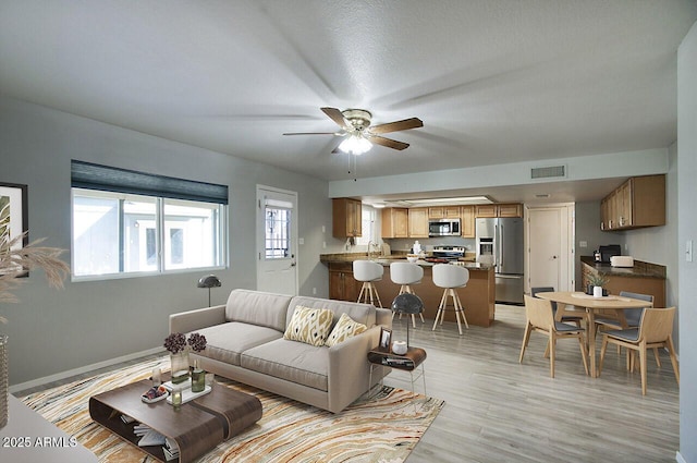 living room with ceiling fan, plenty of natural light, sink, and light wood-type flooring