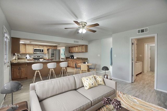 living room featuring sink, ceiling fan, and light wood-type flooring