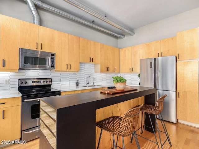 kitchen with stainless steel appliances, light brown cabinetry, a kitchen bar, and sink