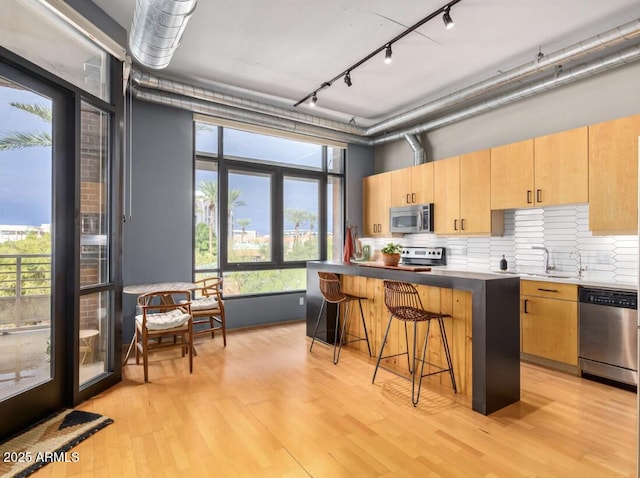 kitchen featuring stainless steel appliances, a center island, a breakfast bar, light hardwood / wood-style flooring, and backsplash