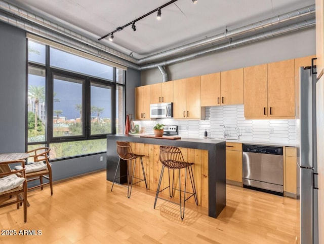 kitchen featuring light hardwood / wood-style flooring, track lighting, a kitchen island, appliances with stainless steel finishes, and a kitchen breakfast bar