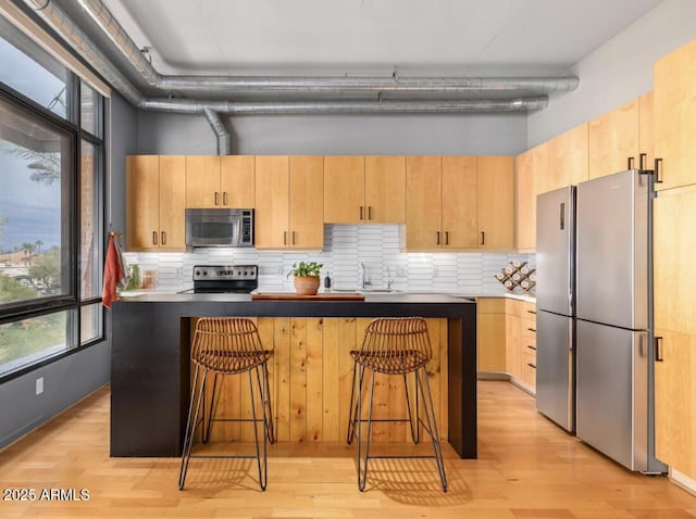 kitchen with stainless steel appliances, a kitchen bar, light brown cabinetry, and a center island