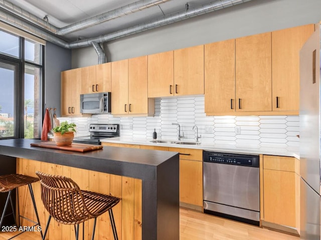 kitchen with stainless steel appliances, sink, light brown cabinets, light wood-type flooring, and a breakfast bar