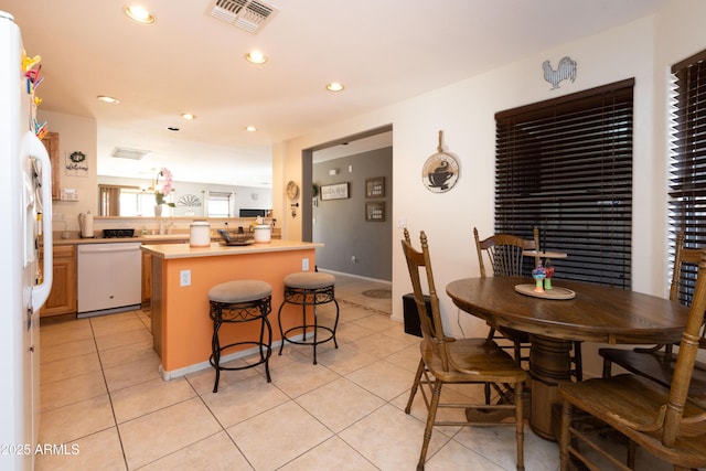 kitchen with light tile patterned flooring, white appliances, a breakfast bar, and kitchen peninsula