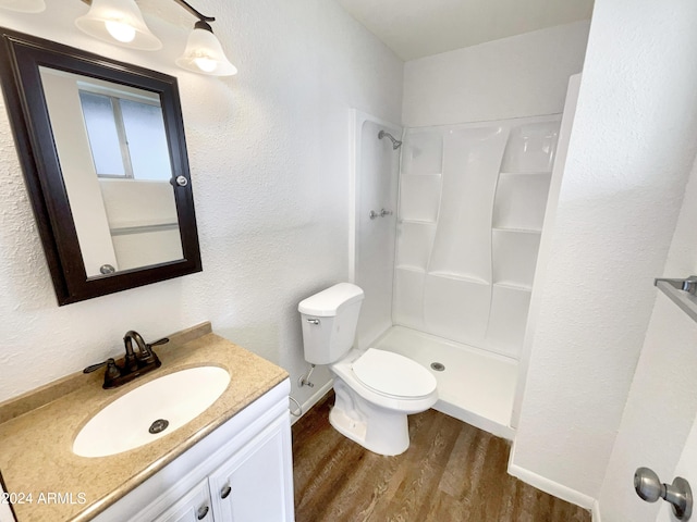 full bathroom featuring a textured wall, toilet, wood finished floors, vanity, and walk in shower