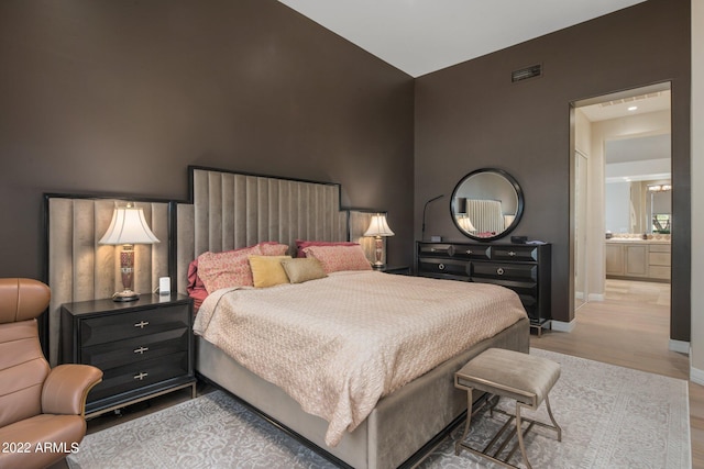 bedroom with connected bathroom and light hardwood / wood-style flooring