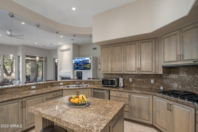 kitchen with pendant lighting, stainless steel appliances, ceiling fan, sink, and light stone counters