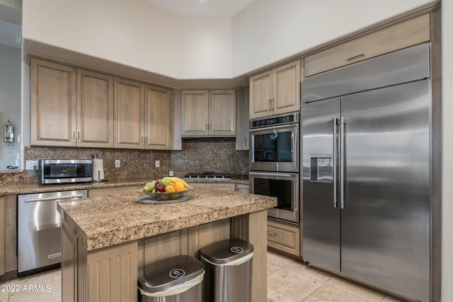 kitchen featuring a kitchen island, light tile floors, tasteful backsplash, appliances with stainless steel finishes, and light stone counters