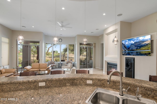 kitchen with decorative light fixtures, ceiling fan, sink, and light stone counters