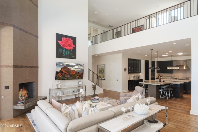 living room with light hardwood / wood-style floors, a tile fireplace, and a towering ceiling