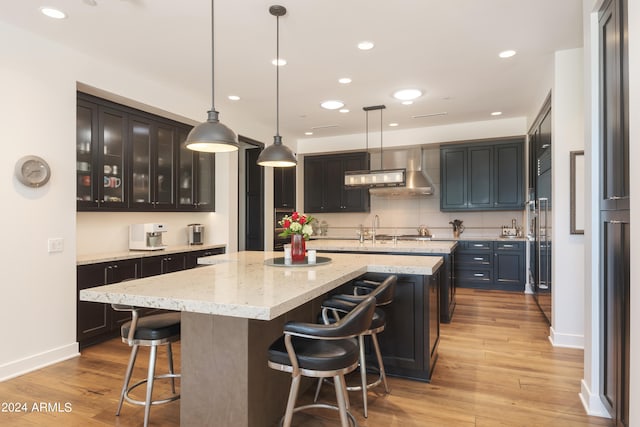 kitchen featuring wall chimney exhaust hood, a kitchen breakfast bar, light hardwood / wood-style flooring, and pendant lighting