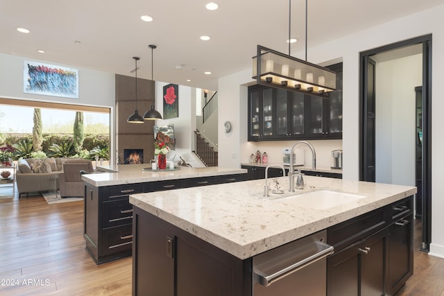 kitchen featuring sink, decorative light fixtures, a center island with sink, and light wood-type flooring