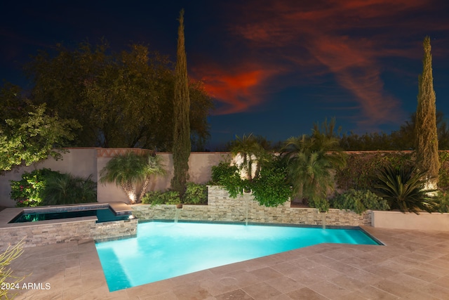 pool at night featuring a patio area, pool water feature, and an in ground hot tub